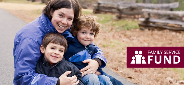 mother outdoors holding two young boys, all wearing jackets