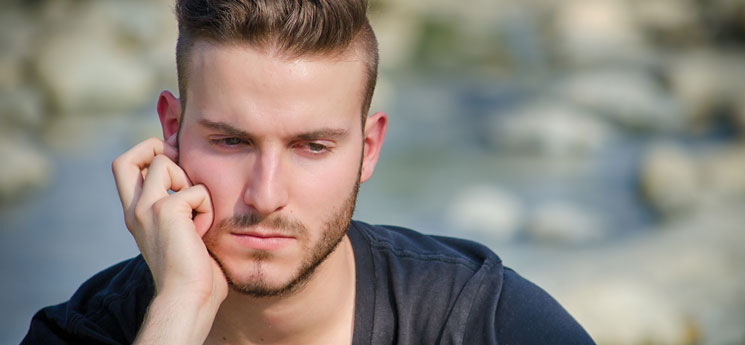 young, sad, pensive man looking down with and resting on face