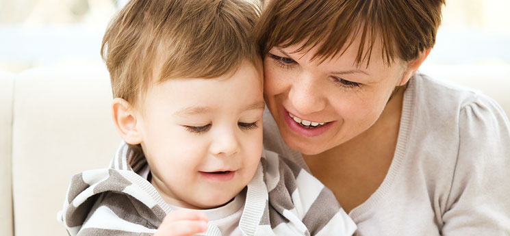 young mom looking down at book while reading with her toddler son