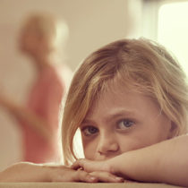 young girl looking at camera while parents argue in background