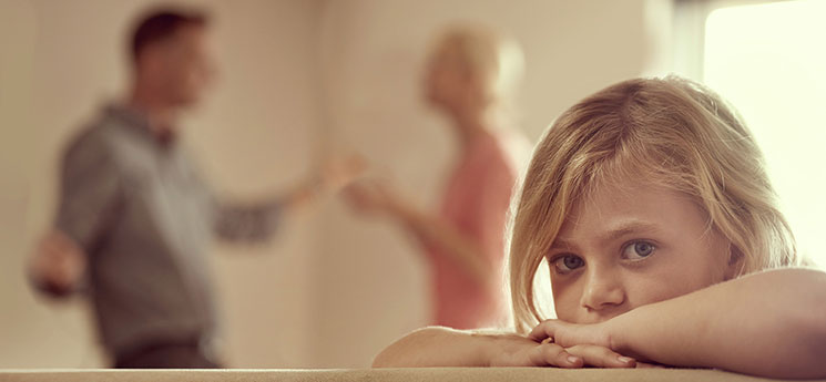 young girl looking at camera while parents argue in background